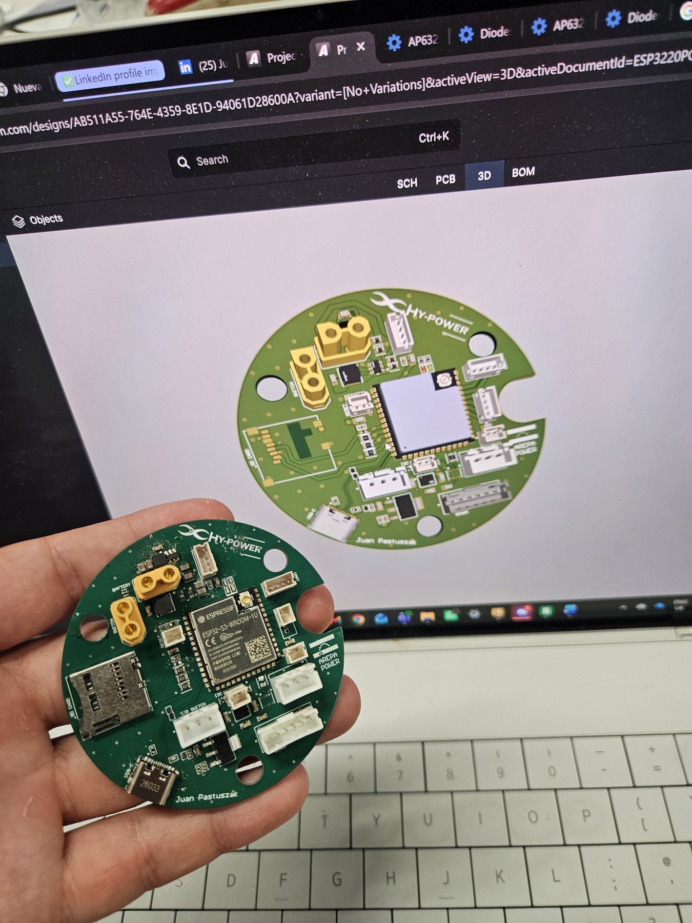 The assembled board held in a hand in front of its 3D model on a laptop screen