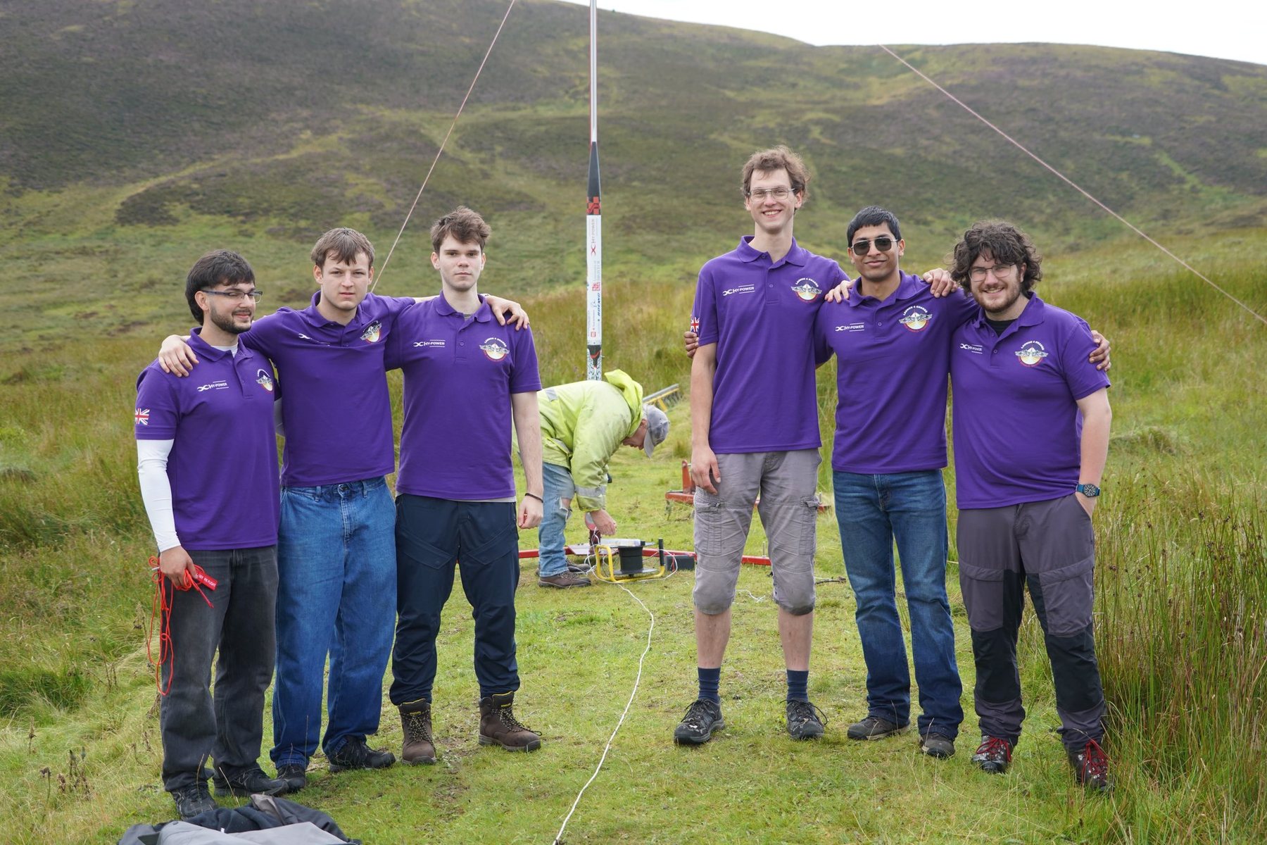 Six members of HyPower Bristol in purple team shirts beside the rocket on its launch rail on a hillside